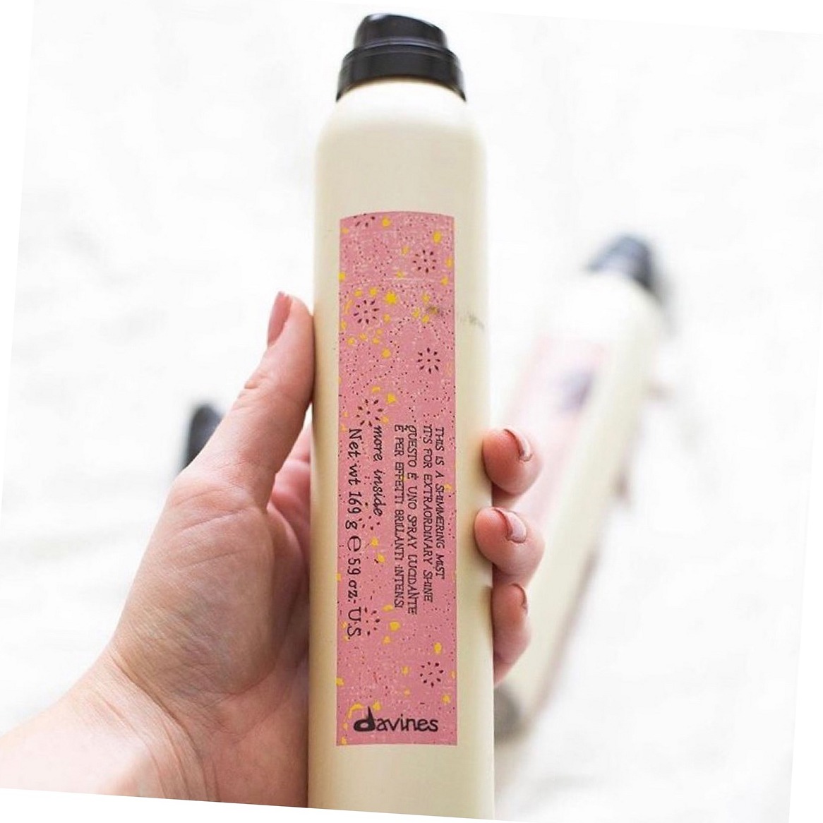 Een fles Davines met een roze etiket, rechtop in de hand gehouden